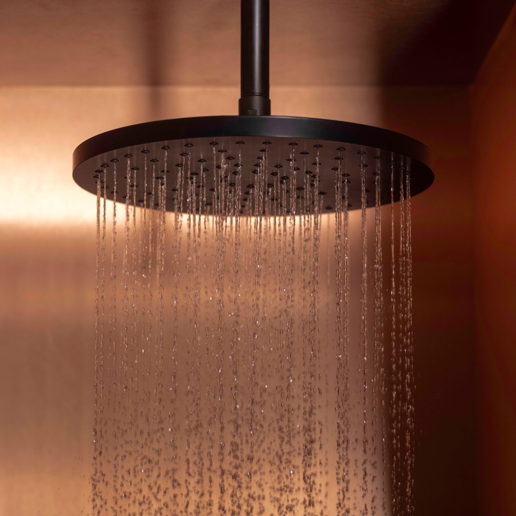 Lifestyle image of the Roca RainSense Matt Black 250mm Round Shower Head mounted on a ceiling with water flowing down
